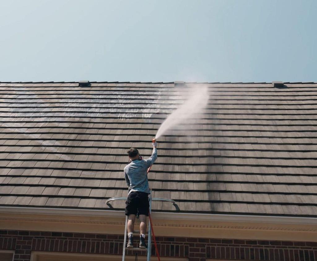 Roof being soft washed from a ladder